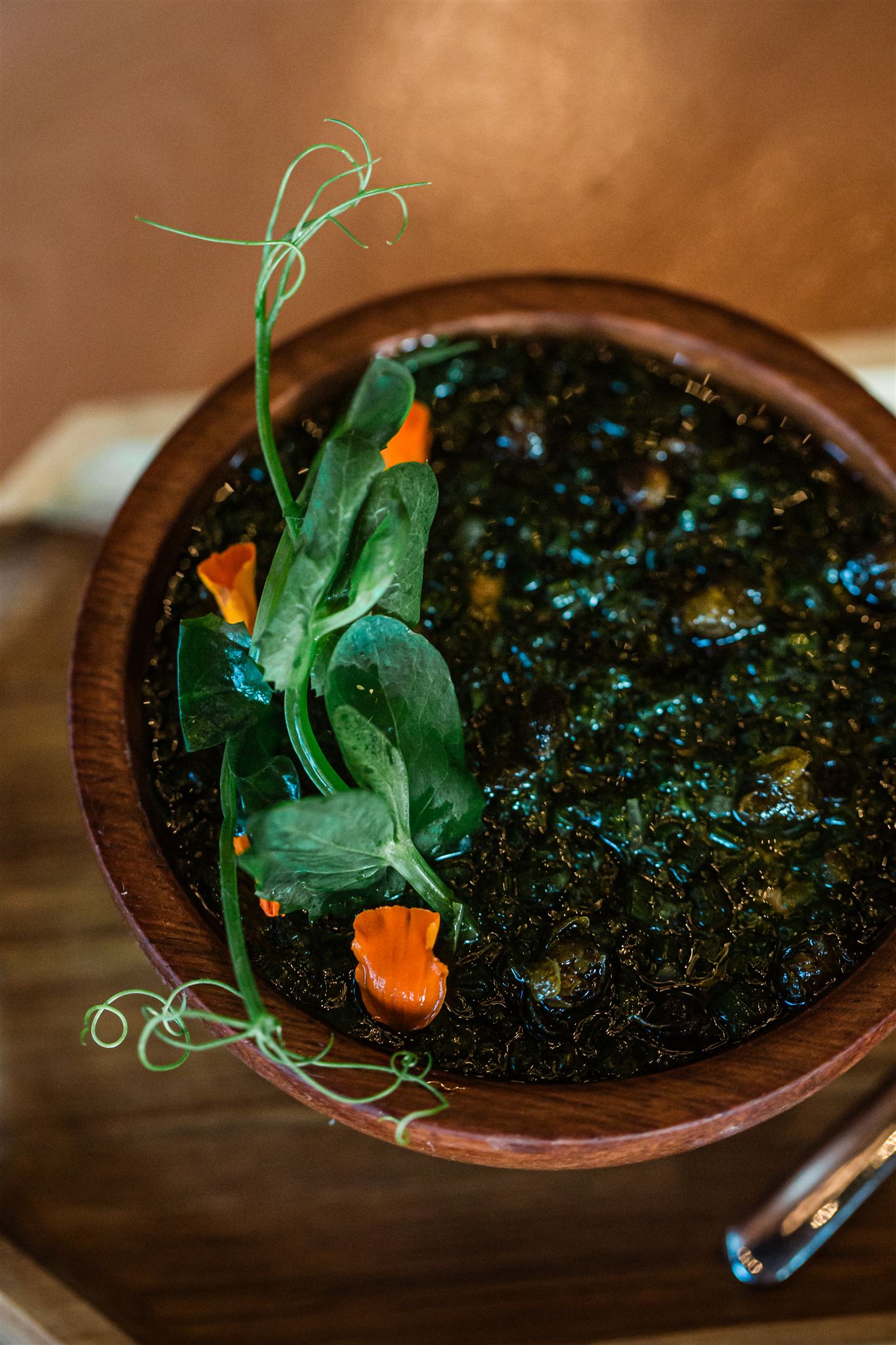 Dish in a wooden bowl with pea shoots and nasturtium